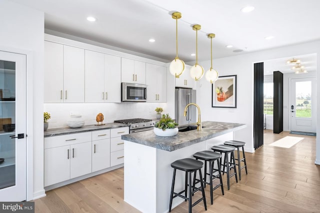 kitchen with light wood finished floors, a sink, stainless steel appliances, a breakfast bar area, and an island with sink