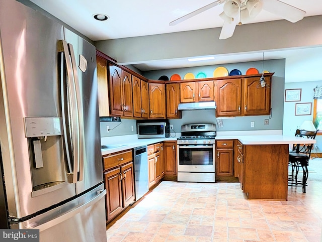 kitchen with under cabinet range hood, a peninsula, brown cabinets, and appliances with stainless steel finishes
