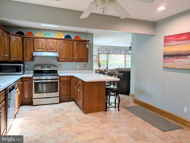 kitchen with appliances with stainless steel finishes, a breakfast bar, a peninsula, a ceiling fan, and under cabinet range hood