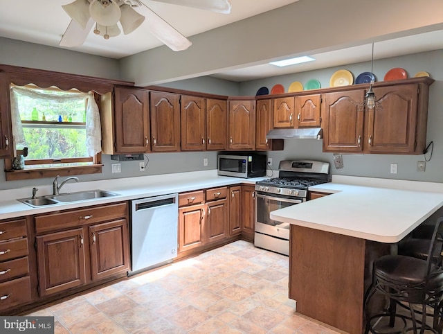 kitchen featuring a kitchen breakfast bar, a sink, a peninsula, under cabinet range hood, and stainless steel appliances