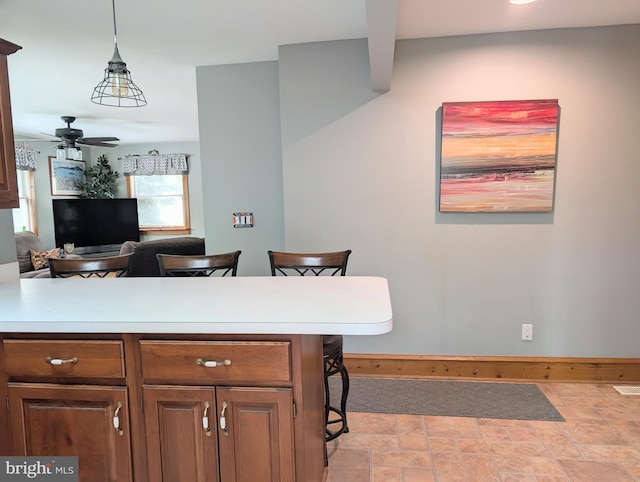kitchen with a ceiling fan, stone finish flooring, decorative light fixtures, light countertops, and a peninsula