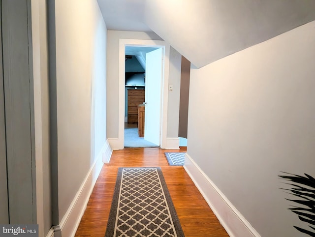 hall featuring baseboards, wood finished floors, and vaulted ceiling