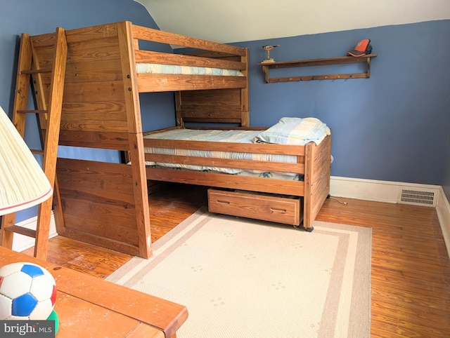 bedroom with baseboards, lofted ceiling, wood finished floors, and visible vents