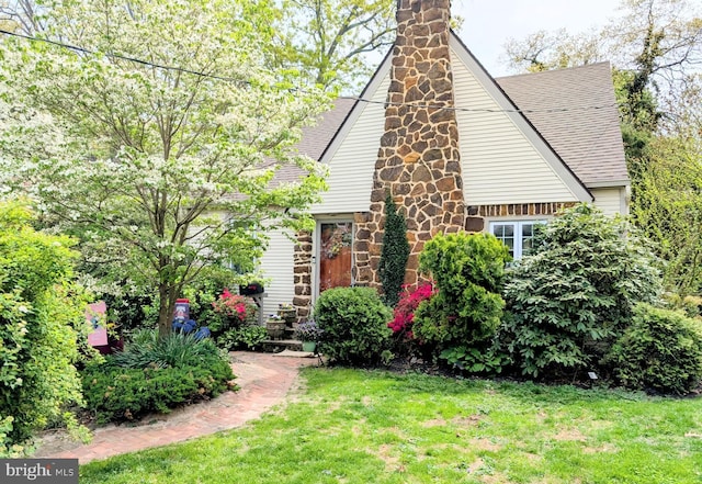 view of front of house with roof with shingles, stone siding, and a front yard