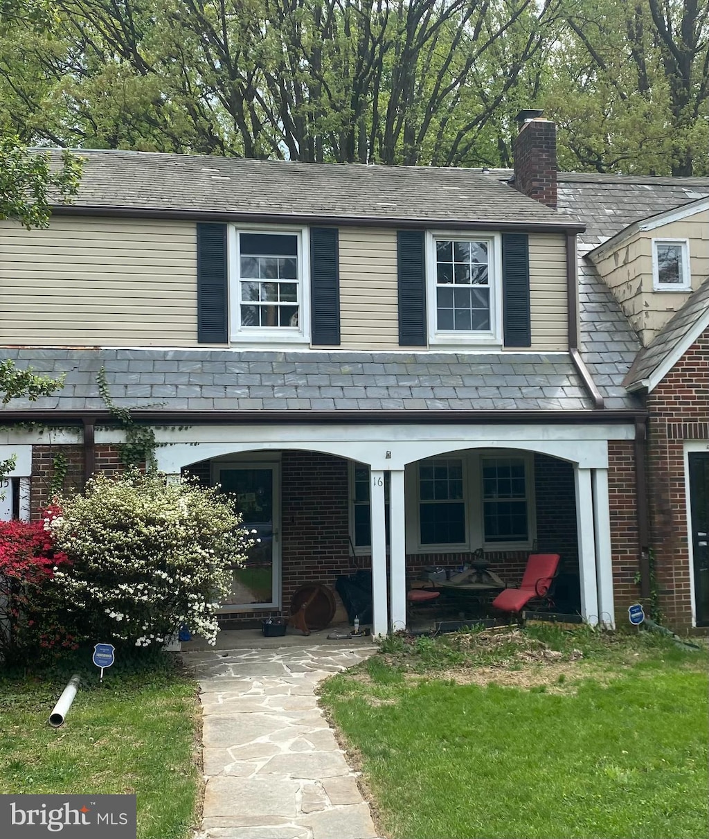 traditional-style home with brick siding, a high end roof, a chimney, and a patio