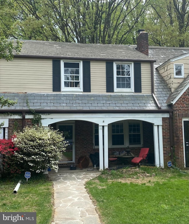 traditional-style home with brick siding, a high end roof, a chimney, and a patio