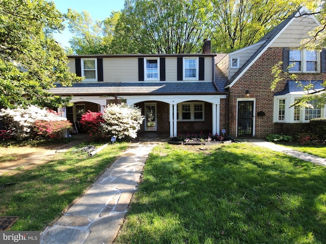 view of front facade featuring covered porch, a chimney, a front lawn, and brick siding