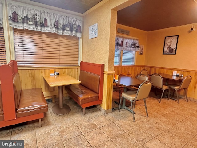 tiled dining room featuring crown molding, wooden walls, and wainscoting