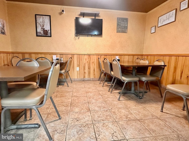 dining room featuring ornamental molding, a wainscoted wall, wooden walls, and a textured wall