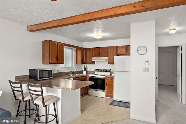 kitchen with dark countertops, a sink, white appliances, a peninsula, and under cabinet range hood