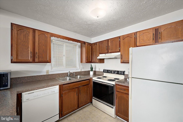 kitchen featuring brown cabinetry, dark countertops, white appliances, under cabinet range hood, and a sink