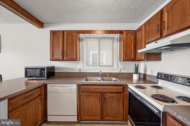 kitchen featuring dark countertops, white appliances, a textured ceiling, under cabinet range hood, and a sink