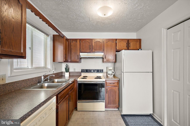 kitchen featuring dark countertops, white appliances, a textured ceiling, under cabinet range hood, and a sink