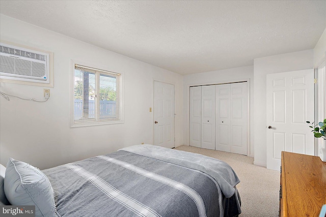 bedroom featuring an AC wall unit, a textured ceiling, a closet, and light colored carpet