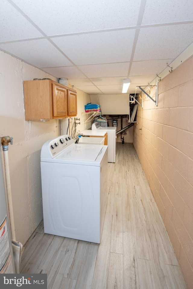laundry area featuring water heater, washer and clothes dryer, light wood finished floors, cabinet space, and concrete block wall