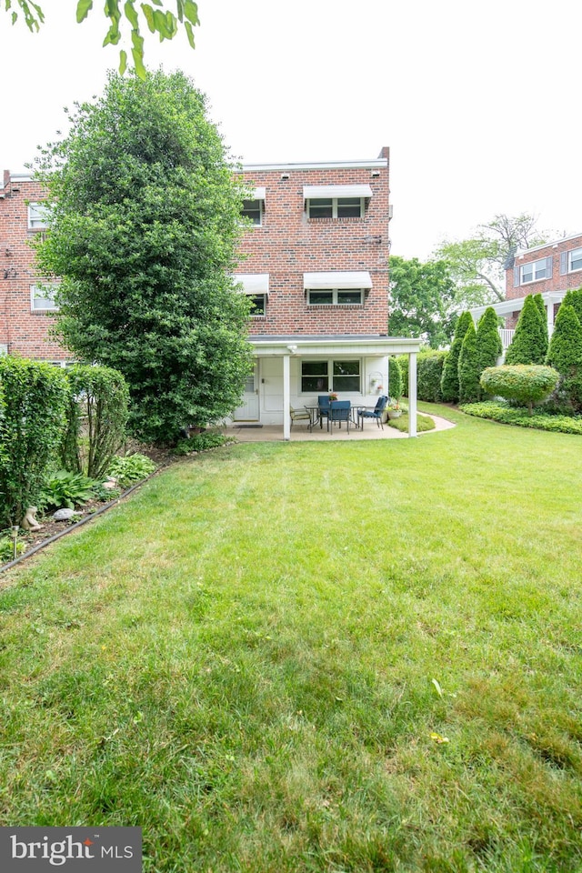 back of house with a patio, brick siding, and a yard