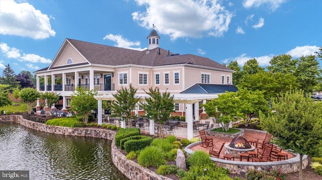 rear view of property with a water view, a balcony, a patio area, and an outdoor fire pit