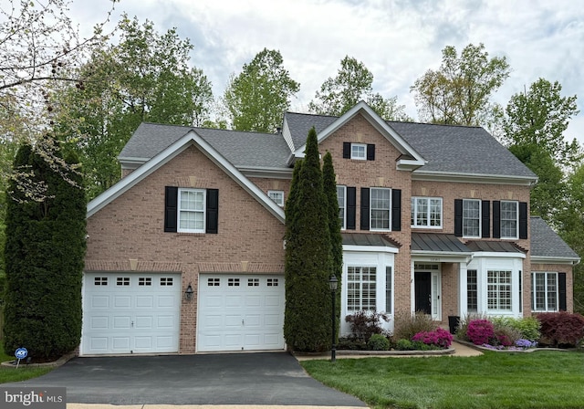 traditional-style house featuring a garage, a front lawn, aphalt driveway, roof with shingles, and brick siding