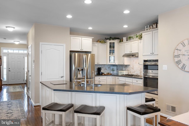 kitchen with tasteful backsplash, under cabinet range hood, appliances with stainless steel finishes, dark countertops, and visible vents