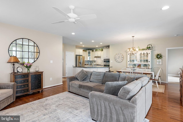 living room featuring baseboards, recessed lighting, wood finished floors, and ceiling fan with notable chandelier