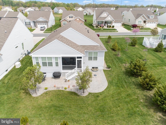 back of house featuring a yard, a shingled roof, a residential view, a sunroom, and a patio area