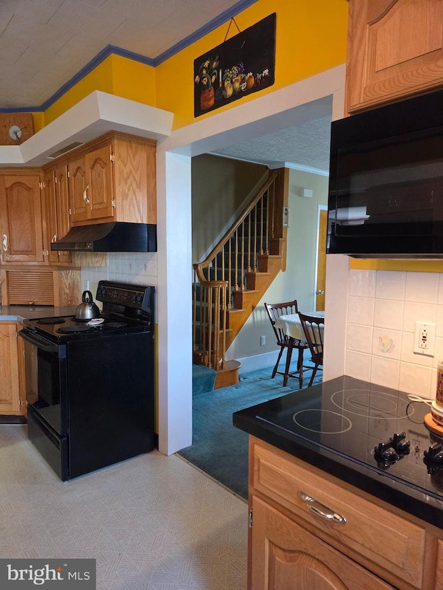 kitchen with crown molding, under cabinet range hood, black appliances, and tasteful backsplash