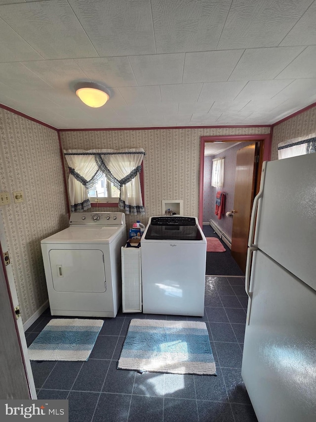 clothes washing area featuring laundry area, baseboard heating, separate washer and dryer, wallpapered walls, and dark tile patterned flooring