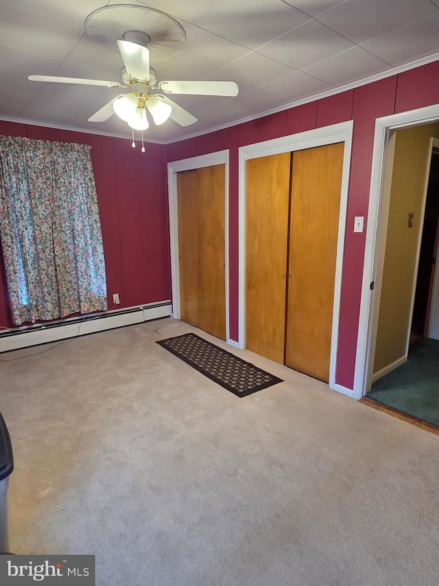 unfurnished bedroom featuring crown molding, a baseboard heating unit, multiple closets, and carpet