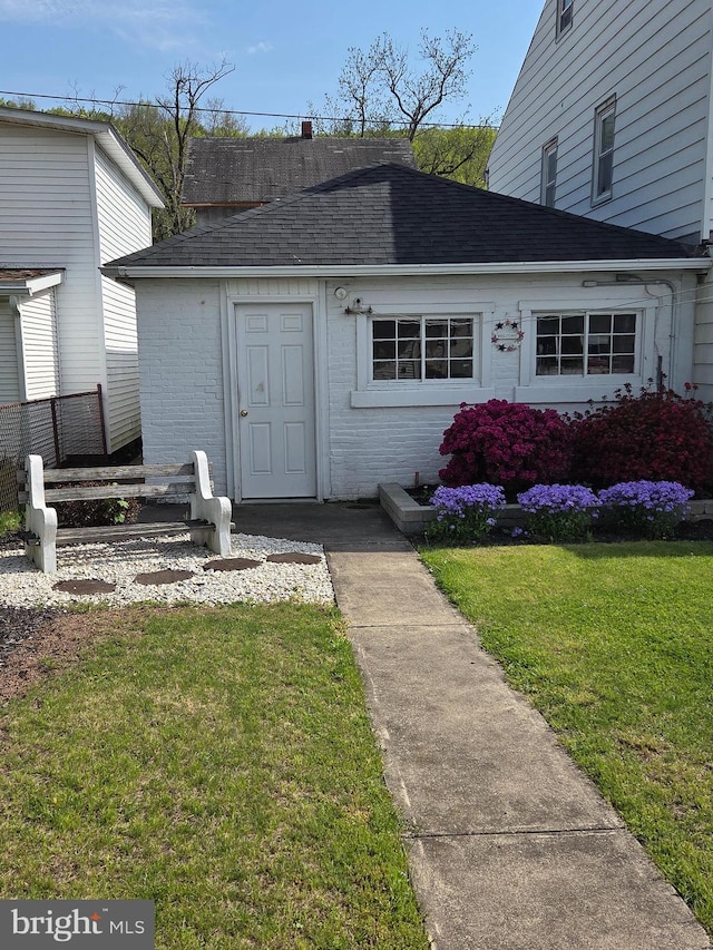 entrance to property with a yard, brick siding, and roof with shingles