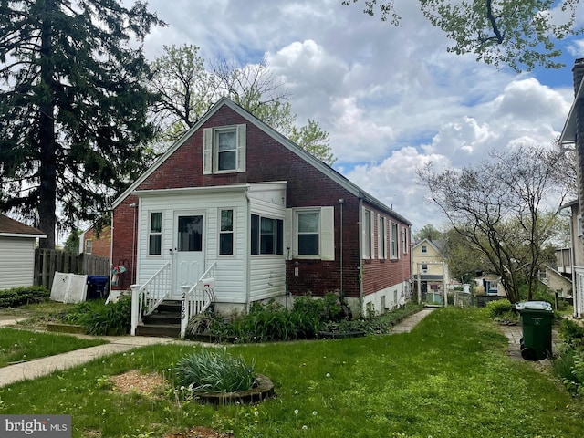 bungalow-style home with brick siding, fence, entry steps, and a front yard