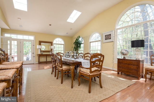 dining room with baseboards, high vaulted ceiling, a skylight, and light wood finished floors
