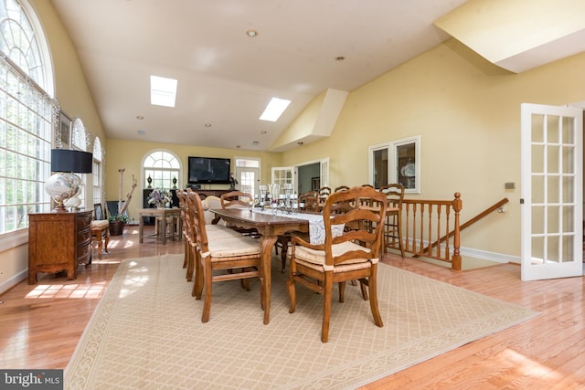dining space with light wood-style floors, baseboards, high vaulted ceiling, and a skylight