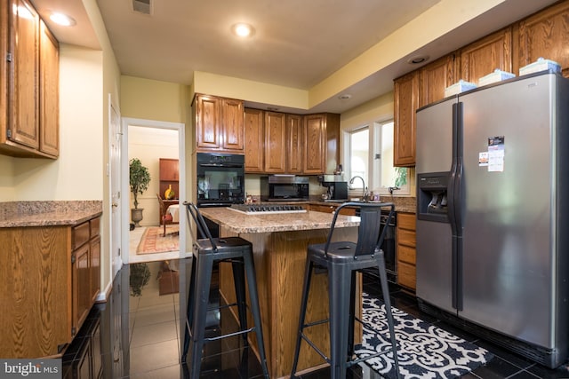 kitchen featuring stainless steel appliances, brown cabinetry, a breakfast bar, a kitchen island, and dark tile patterned flooring