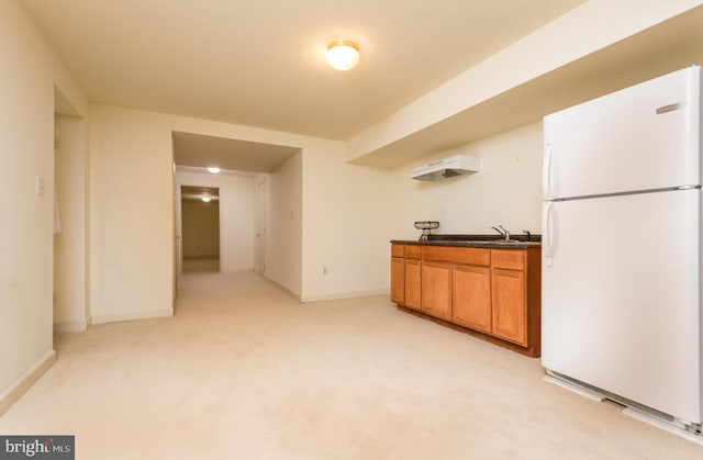 kitchen featuring freestanding refrigerator, brown cabinetry, light carpet, dark countertops, and baseboards