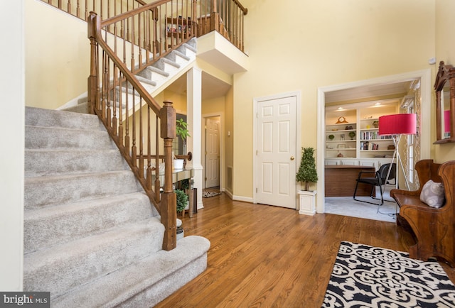 entrance foyer with a towering ceiling, stairs, wood finished floors, and baseboards