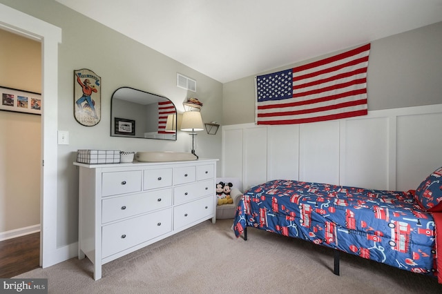 bedroom featuring carpet flooring, visible vents, a decorative wall, and wainscoting