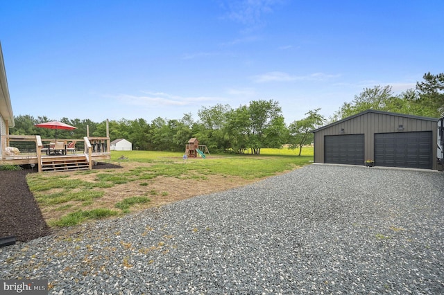 view of yard with a detached garage, an outdoor structure, a playground, and a deck