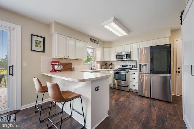 kitchen featuring dark wood finished floors, a peninsula, backsplash, stainless steel appliances, and white cabinets