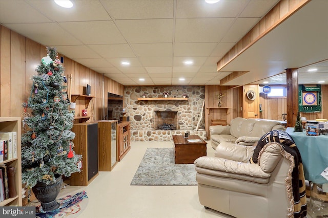 living area with wood walls, a drop ceiling, finished concrete flooring, and a stone fireplace