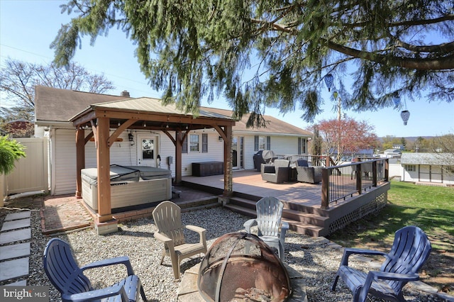exterior space featuring a wooden deck, a hot tub, a gazebo, a fire pit, and fence