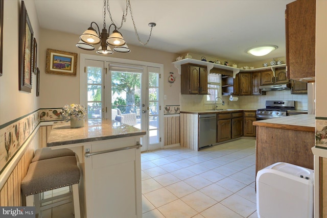 kitchen featuring tasteful backsplash, stainless steel appliances, light countertops, under cabinet range hood, and a notable chandelier