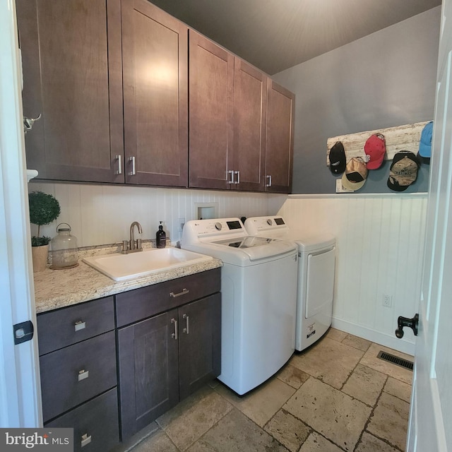 laundry room featuring washing machine and dryer, a sink, visible vents, stone tile flooring, and cabinet space