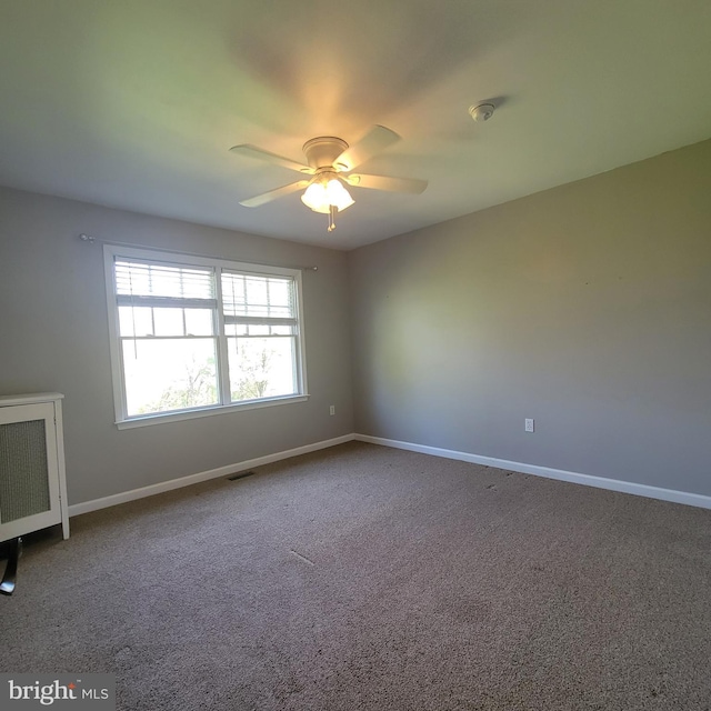 carpeted empty room with radiator, ceiling fan, visible vents, and baseboards