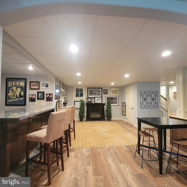 bar with a fireplace, light wood finished floors, a bar, and baseboards