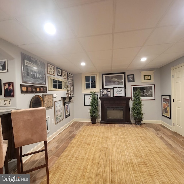 living area featuring baseboards, a glass covered fireplace, recessed lighting, wood finished floors, and a paneled ceiling