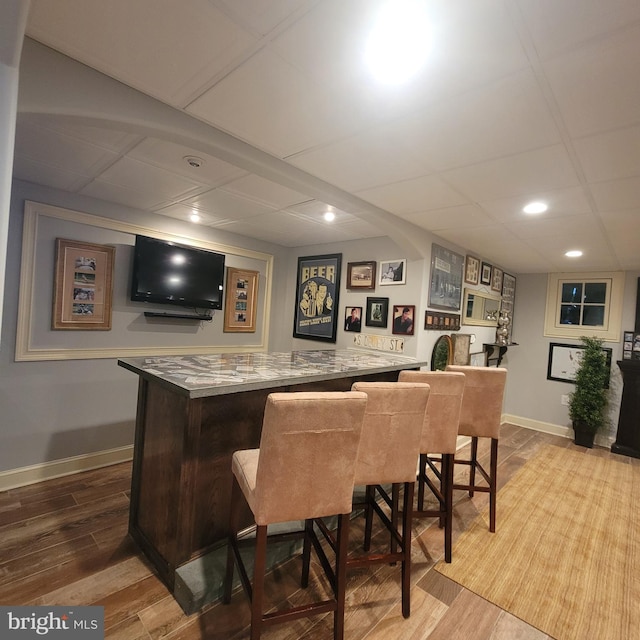 bar featuring baseboards, recessed lighting, wood finished floors, and a bar