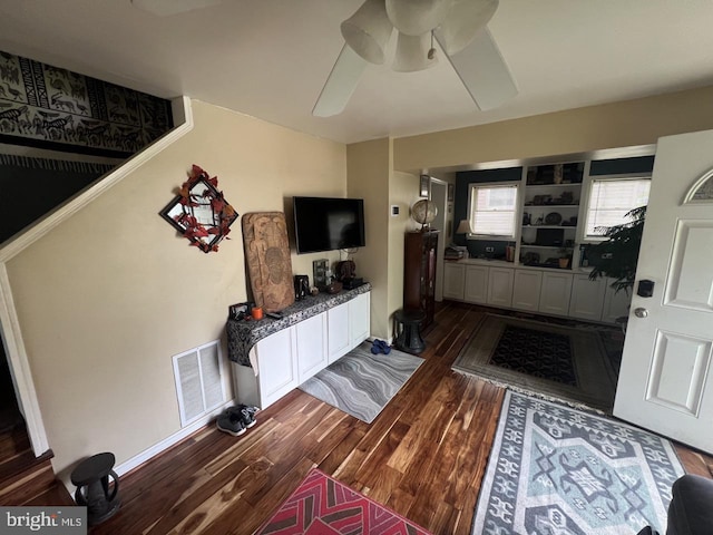 living room with a ceiling fan, visible vents, and dark wood finished floors