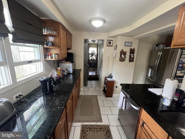 kitchen with open shelves, dark stone counters, brown cabinets, appliances with stainless steel finishes, and light tile patterned floors