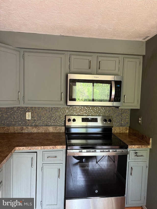 22 Morning Ct, Rosedale, MD 21237 - kitchen featuring dark countertops, a textured ceiling, gray cabinets, stainless steel appliances, and decorative backsplash