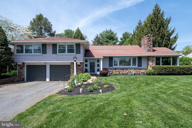 tri-level home featuring a chimney, a garage, aphalt driveway, and stone siding